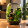 Handcrafted desktop moss terrarium featuring a miniature pagoda and bridge next to a laptop, showcasing a long-lasting living indoor plant gift.