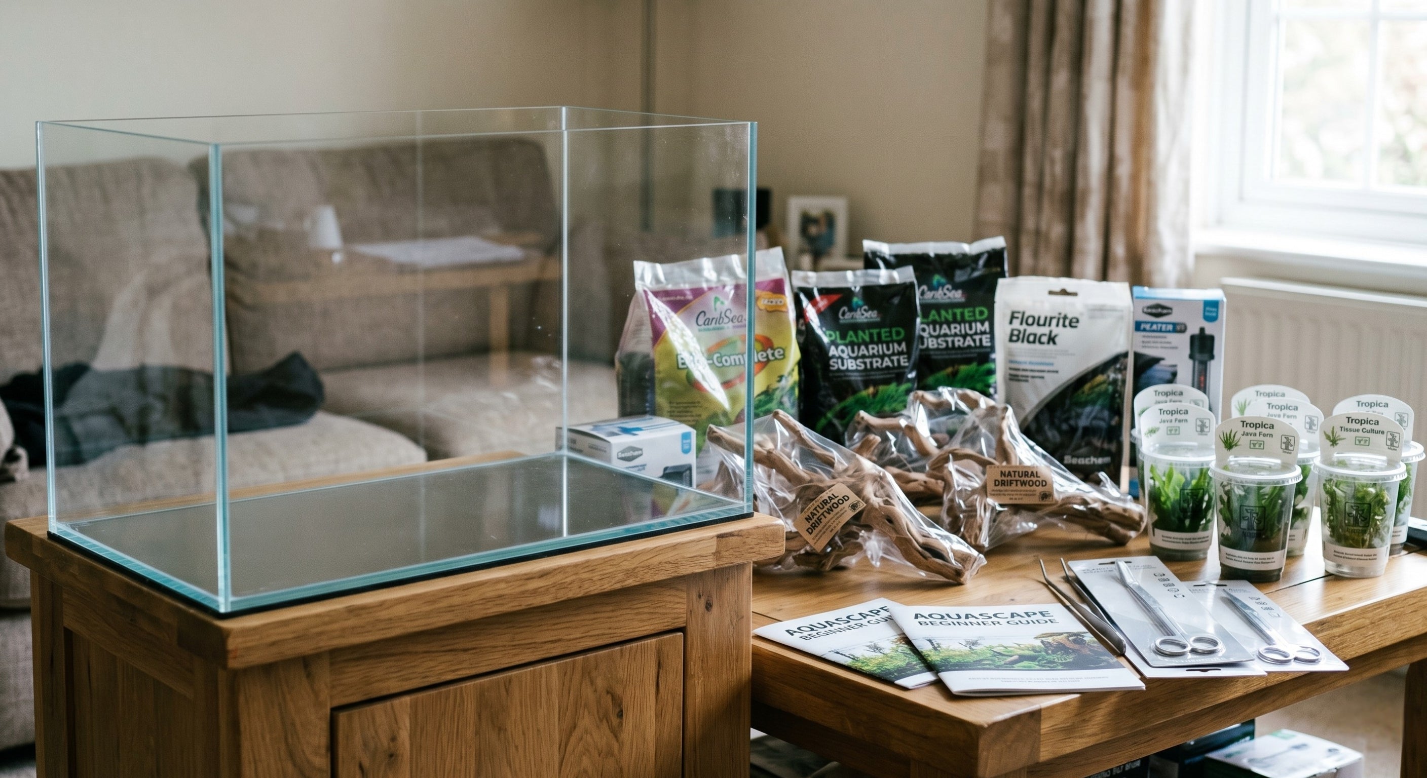 Empty glass aquarium tank on a stand surrounded by unopened aquascaping supplies like substrate, driftwood, and aquatic plants for beginner setup.